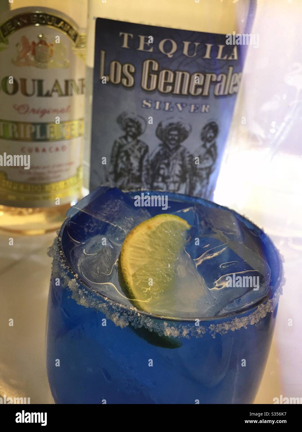 A margarita cocktail in a blue crystal glass in front of bottles of tequila and triple sec Stock