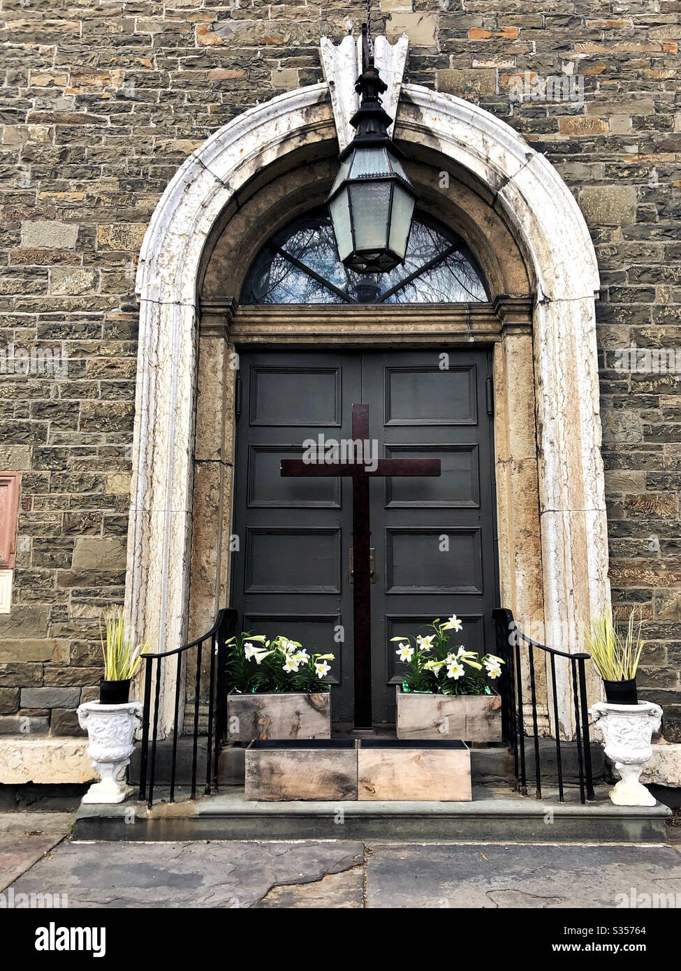 Church closed for Easter with cross and flowers decorating front door Stock Photo