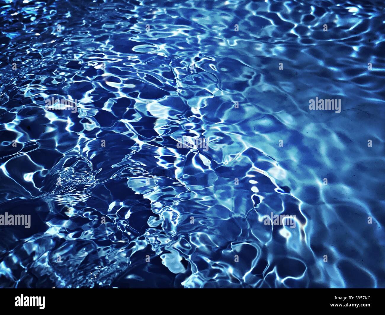 A close up view on the surface of water in a blue swimming pool. Light reflects off gentle ripples creating a colourful summer background pattern. Fresh, clean and vibrant summery vibes. - Smartphone Captured Stock Image