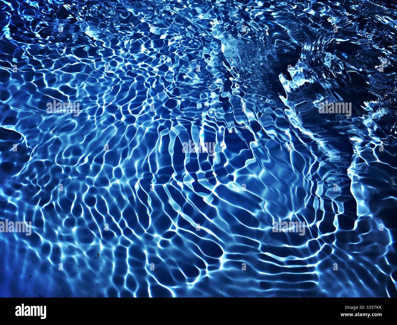 A close up view on the surface of water in a blue swimming pool. Light ...