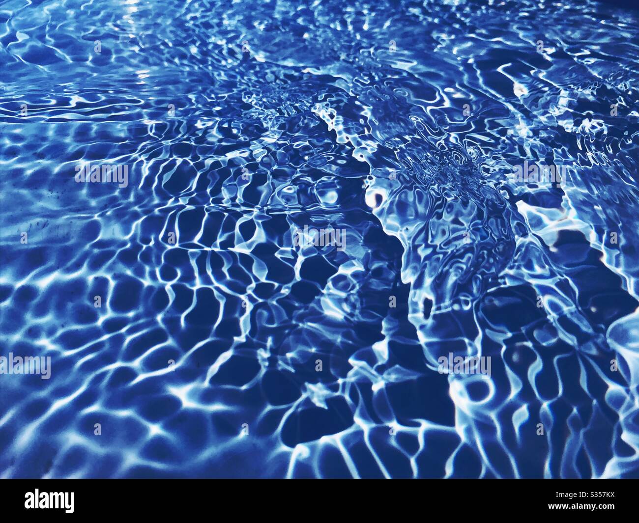 A close up view on the surface of water in a blue swimming pool. Light ...