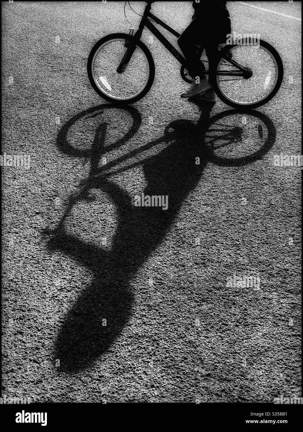 Summer sunshine creates an interesting shadow of a girl as she’s about to ride her bicycle. Copy space if required. Photo credit - ©️ COLIN HOSKINS. - Smartphone Captured Stock Image