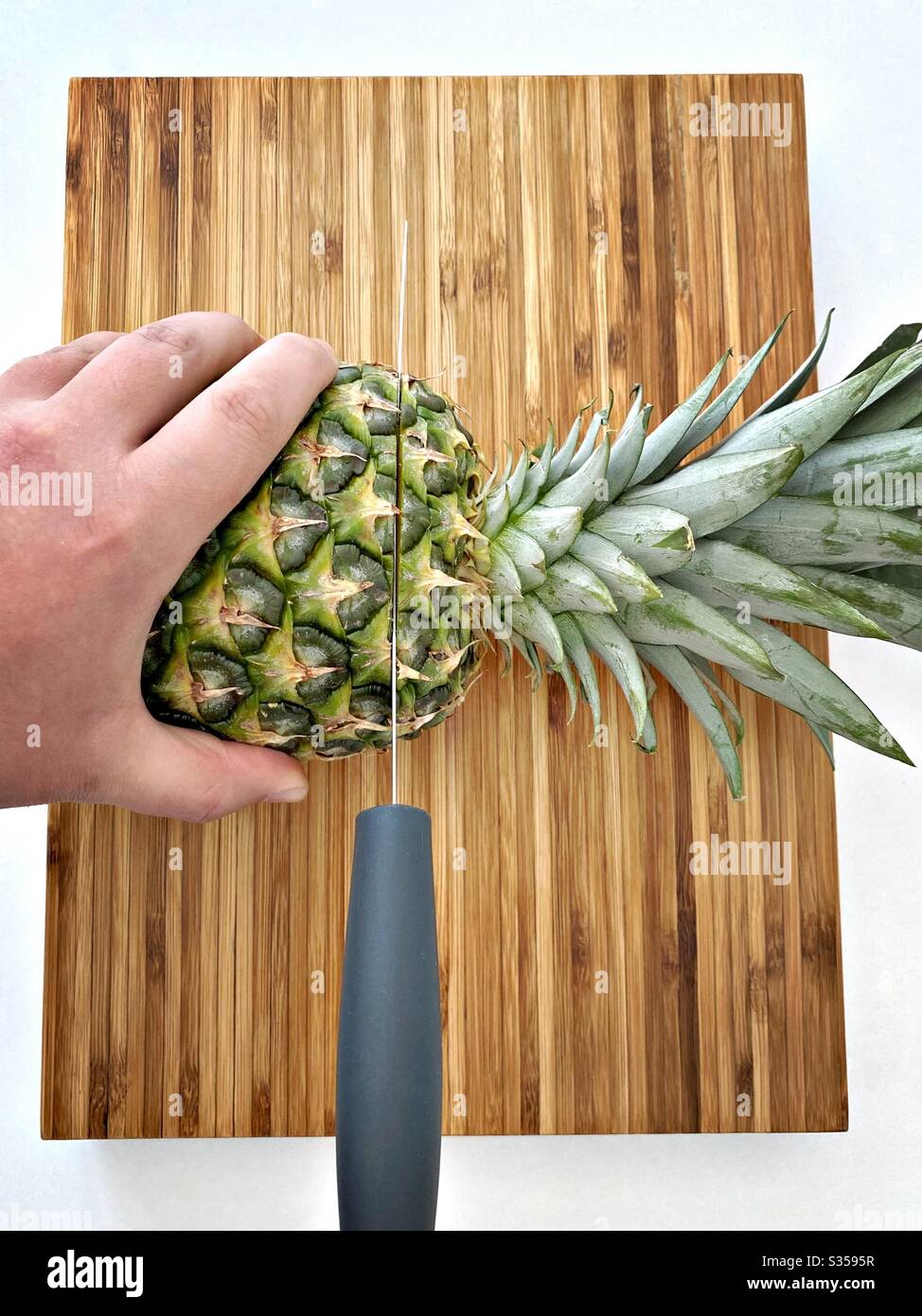 Preparing a whole pineapple in the kitchen. Fresh and ripe fruit preparation. Ingredients for homemade pineapple salsa. On a wooden chopping board with knife - Smartphone Captured Stock Image