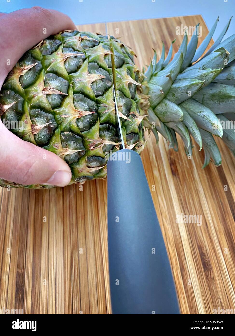 Preparing a whole pineapple in the kitchen. Fresh and ripe fruit preparation. Ingredients for homemade pineapple salsa. On a wooden chopping board with knife - Smartphone Captured Stock Image
