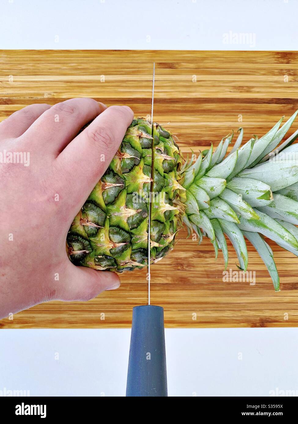 Preparing a whole pineapple in the kitchen. Fresh and ripe fruit preparation. Ingredients for homemade pineapple salsa. On a wooden chopping board with knife - Smartphone Captured Stock Image