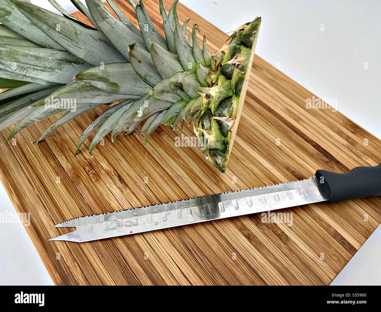 Preparing a whole pineapple in the kitchen. Fresh and ripe fruit preparation. Ingredients for homemade pineapple salsa. On a wooden chopping board with knife - Smartphone Captured Stock Image