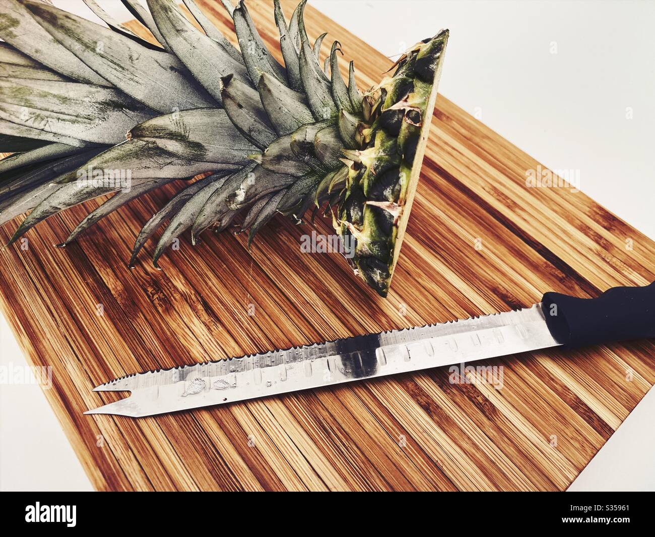 Preparing a whole pineapple in the kitchen. Fresh and ripe fruit preparation. Ingredients for homemade pineapple salsa. On a wooden chopping board with knife - Smartphone Captured Stock Image