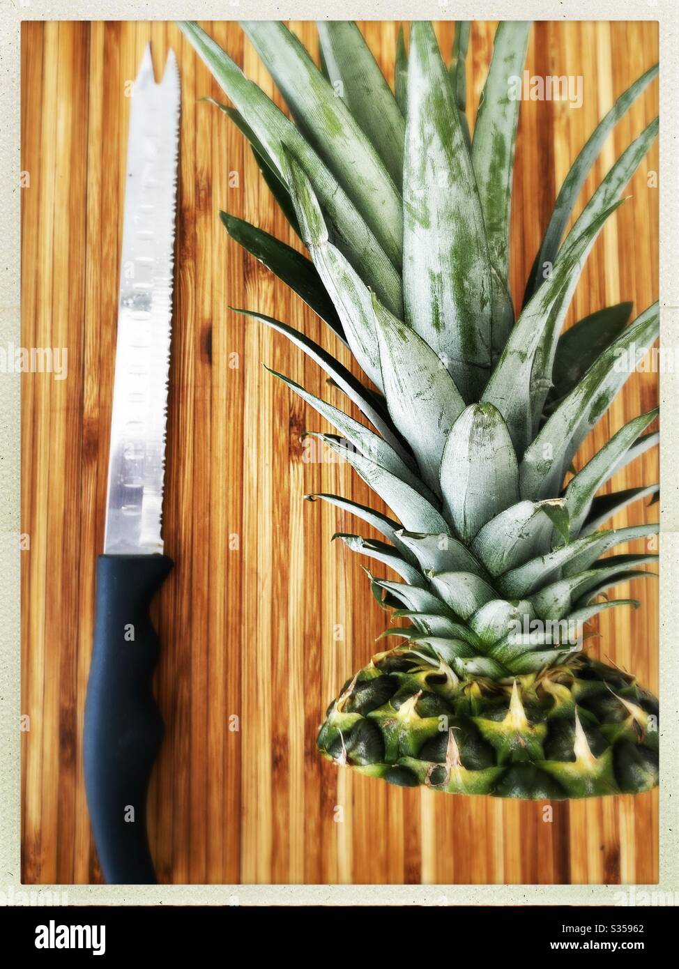 Preparing a whole pineapple in the kitchen. Fresh and ripe fruit preparation. Ingredients for homemade pineapple salsa. On a wooden chopping board with knife - Smartphone Captured Stock Image
