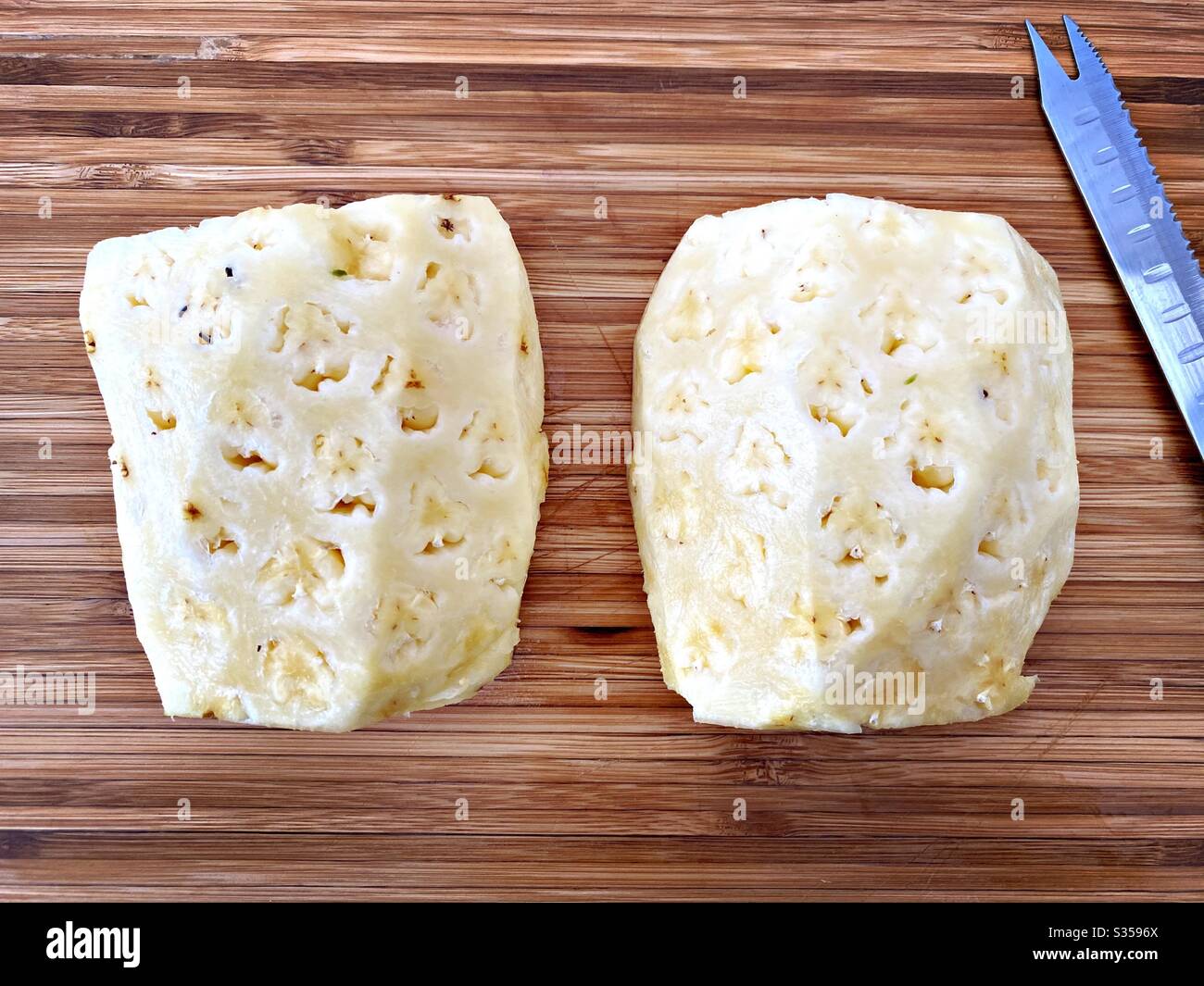 Preparing a whole pineapple in the kitchen. Fresh and ripe fruit preparation. Ingredients for homemade pineapple salsa. On a wooden chopping board. Peeled and halved with eyes removed - Smartphone Captured Stock Image