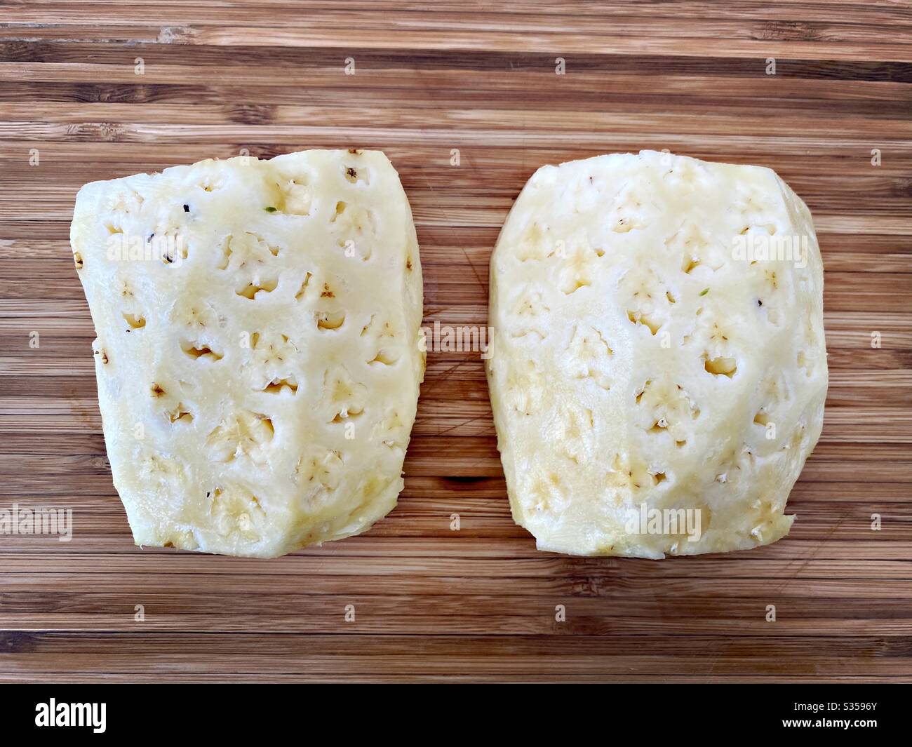 Preparing a whole pineapple in the kitchen. Fresh and ripe fruit preparation. Ingredients for homemade pineapple salsa. On a wooden chopping board. Peeled and halved with eyes removed - Smartphone Captured Stock Image