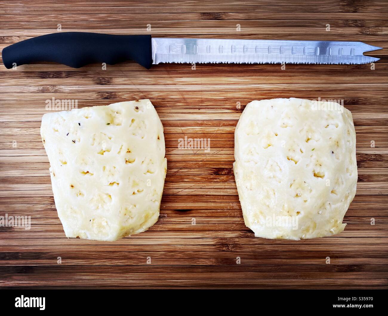 Preparing a whole pineapple in the kitchen. Fresh and ripe fruit preparation. Ingredients for homemade pineapple salsa. On a wooden chopping board. Peeled and halved with eyes removed - Smartphone Captured Stock Image
