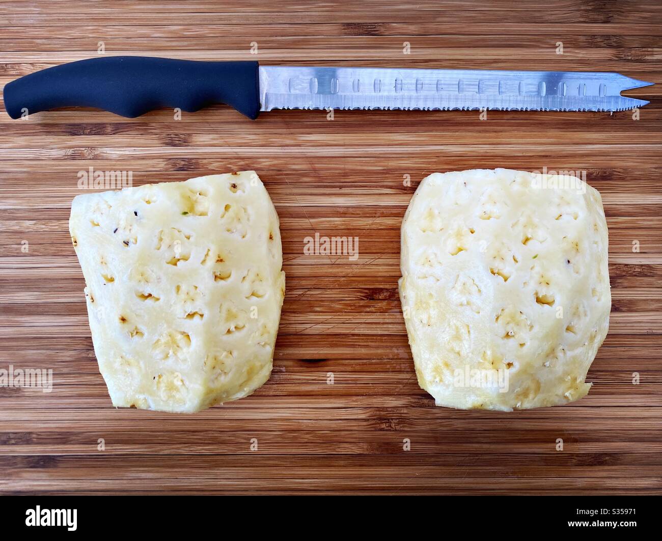 Preparing a whole pineapple in the kitchen. Fresh and ripe fruit preparation. Ingredients for homemade pineapple salsa. On a wooden chopping board. Peeled and halved with eyes removed - Smartphone Captured Stock Image