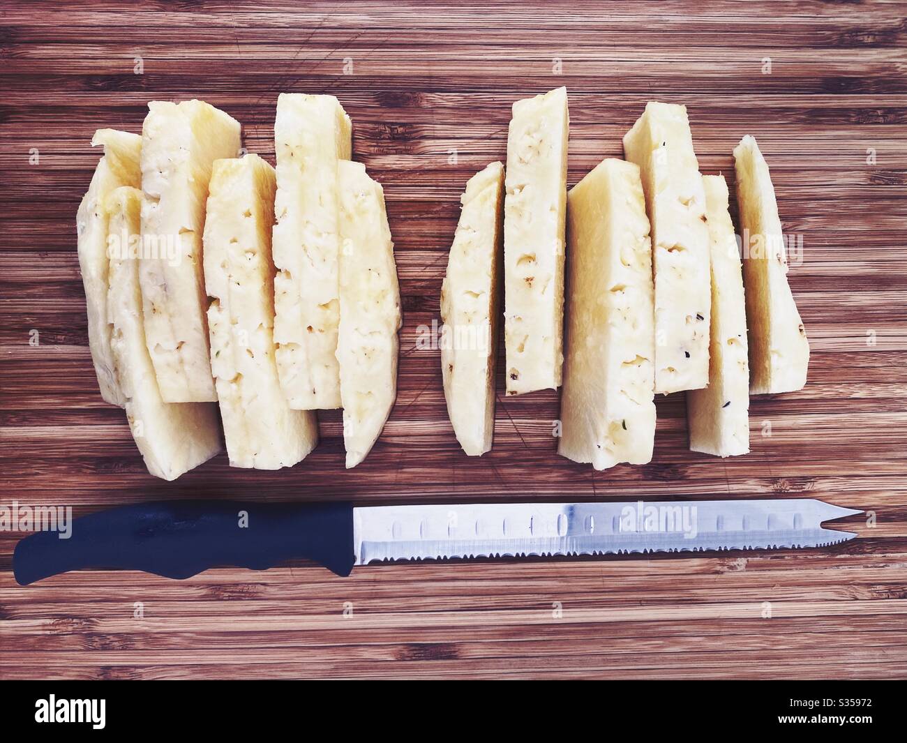 Preparing a whole pineapple in the kitchen. Fresh and ripe fruit preparation. Ingredients for homemade pineapple salsa. On a wooden chopping board. Peeled and sliced with eyes removed - Smartphone Captured Stock Image