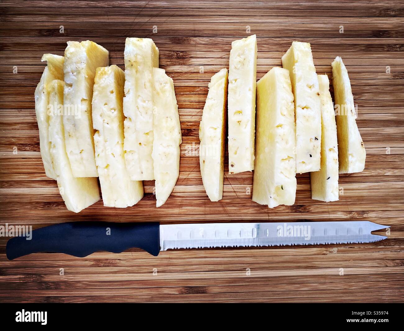 Preparing a whole pineapple in the kitchen. Fresh and ripe fruit preparation. Ingredients for homemade pineapple salsa. On a wooden chopping board. Peeled and sliced with eyes removed - Smartphone Captured Stock Image