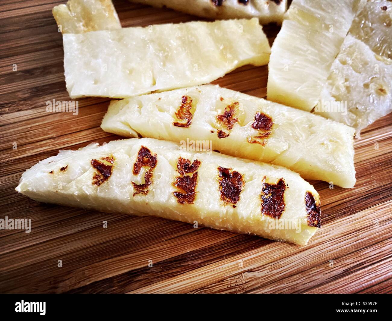 Preparing a whole pineapple in the kitchen. Fresh and ripe fruit preparation. Ingredients for homemade pineapple salsa. Chargrilled slices on a wooden chopping board, closeup view. - Smartphone Captured Stock Image