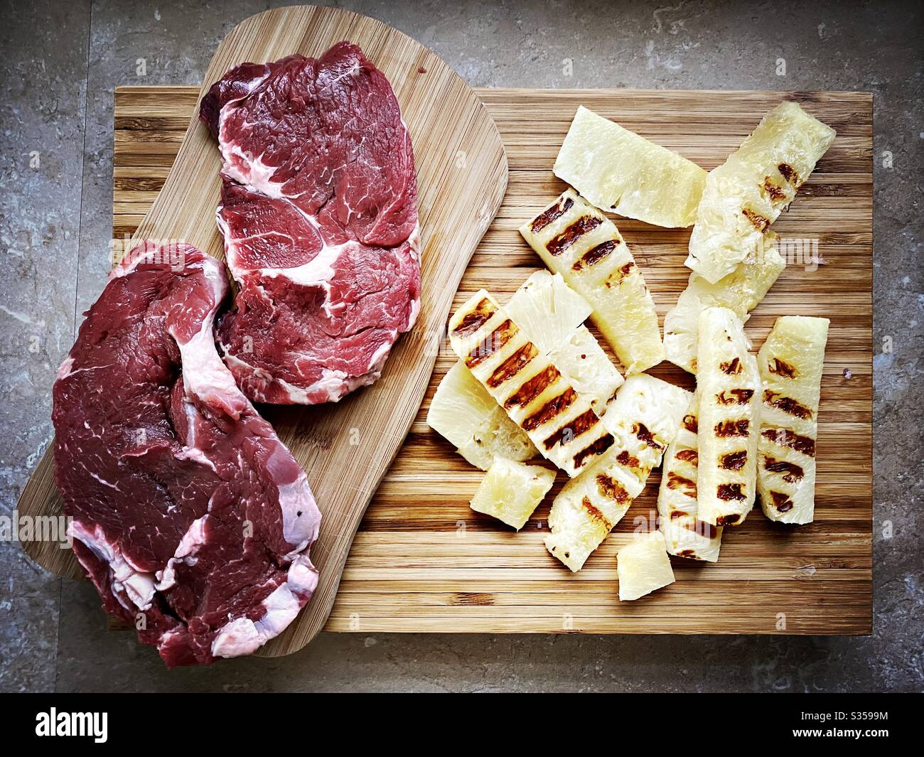 Preparing dinner in the kitchen. Fresh food preparation. Ingredients for homemade pineapple salsa. Chargrilled slices on a wooden chopping board with two ribeye steaks - Smartphone Captured Stock Image