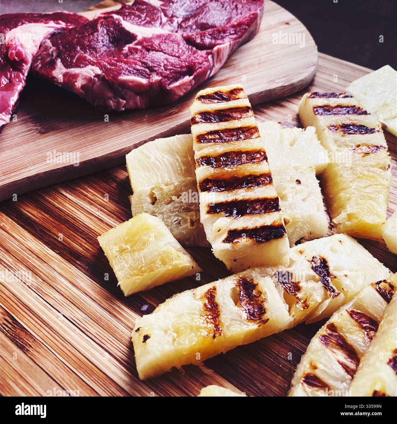 Preparing dinner in the kitchen. Fresh food preparation. Ingredients for homemade pineapple salsa. Chargrilled slices on a wooden chopping board with two ribeye steaks - Smartphone Captured Stock Image