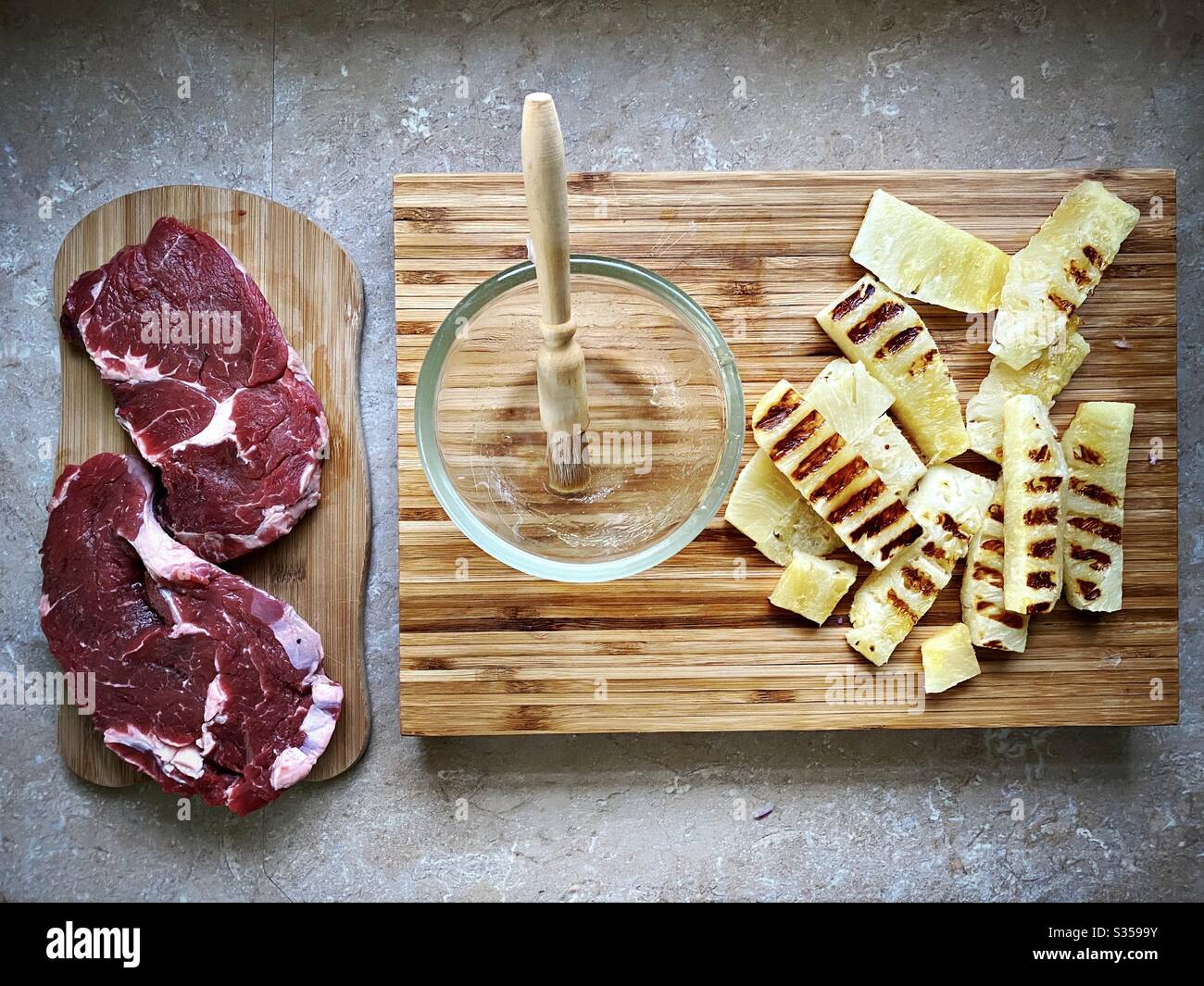 Preparing dinner in the kitchen. Fresh food preparation. Ingredients for homemade pineapple salsa. Chargrilled slices on a wooden chopping board with two ribeye steaks and honey marinade - Smartphone Captured Stock Image