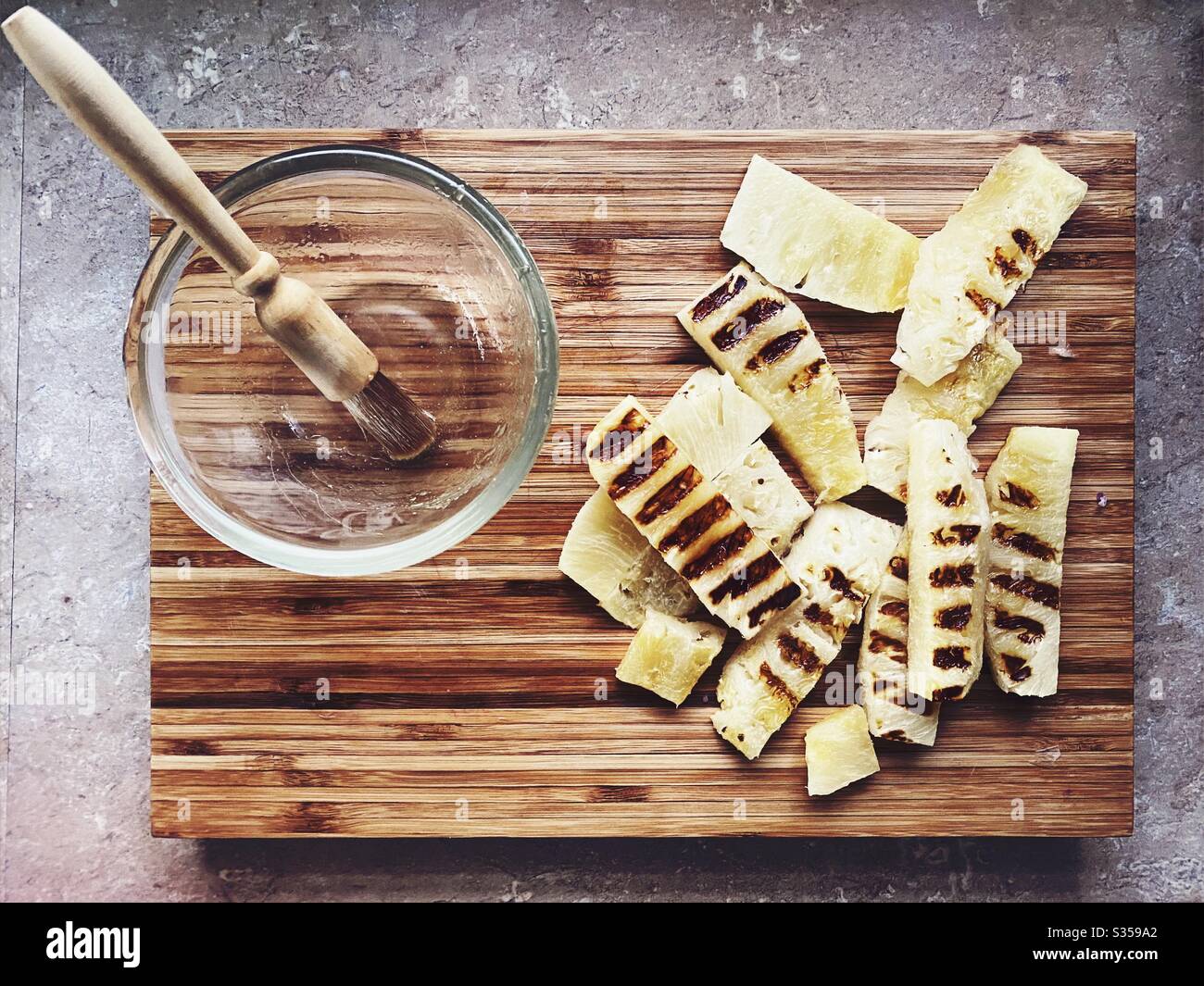 Preparing dinner in the kitchen. Fresh food preparation. Ingredients for homemade pineapple salsa. Chargrilled slices on a wooden chopping board and honey marinade - Smartphone Captured Stock Image