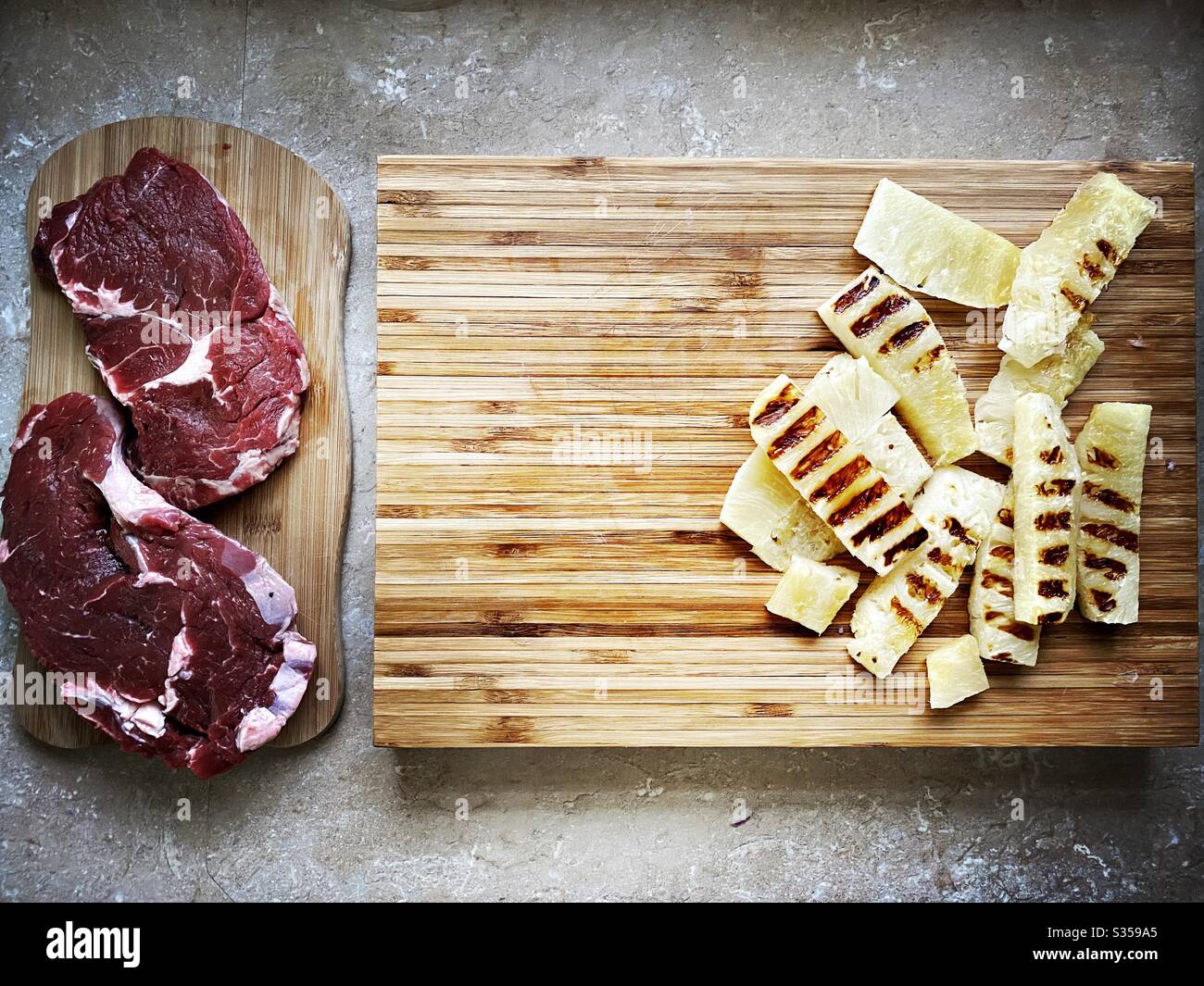 Preparing dinner in the kitchen. Fresh food preparation. Ingredients for homemade pineapple salsa. Chargrilled slices on a wooden chopping board with two ribeye steaks - Smartphone Captured Stock Image