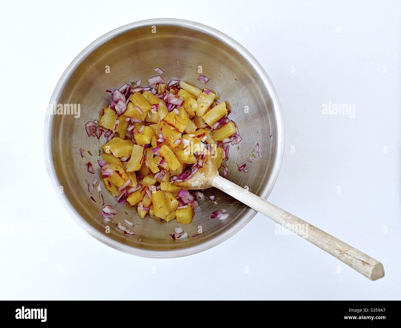Preparing pineapple dish in the kitchen. Fresh and ripe fruit preparation. Ingredients for homemade pineapple salsa. Chargrilled chunks with red onion, lime juice and coriander in a steel mixing bowl. - Smartphone Captured Stock Image