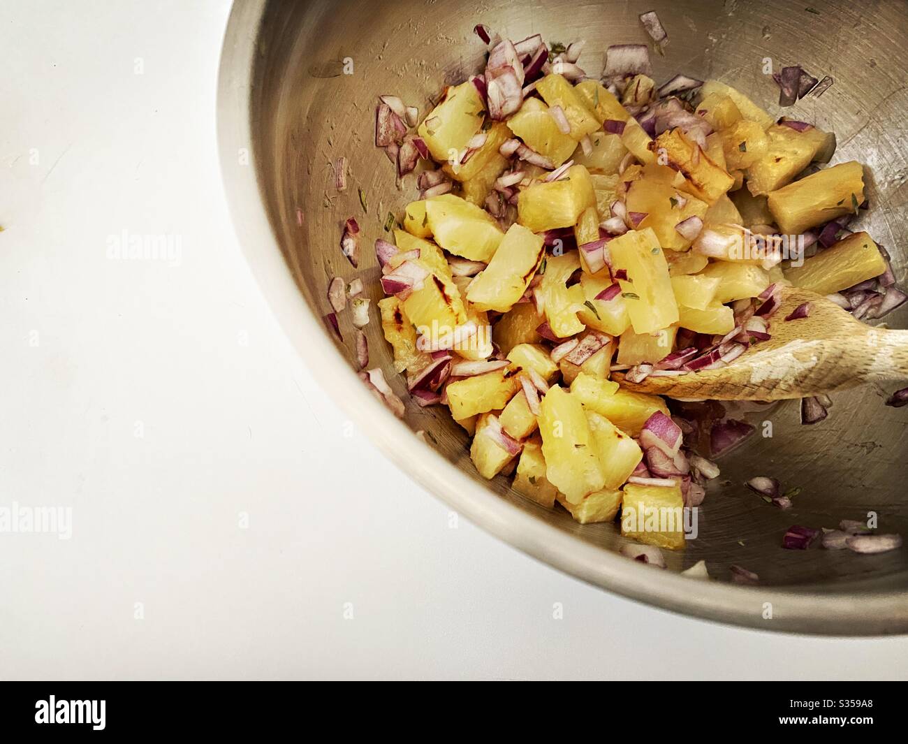 Preparing pineapple dish in the kitchen. Fresh and ripe fruit preparation. Ingredients for homemade pineapple salsa. Chargrilled chunks with red onion, lime juice and coriander in a steel mixing bowl. - Smartphone Captured Stock Image