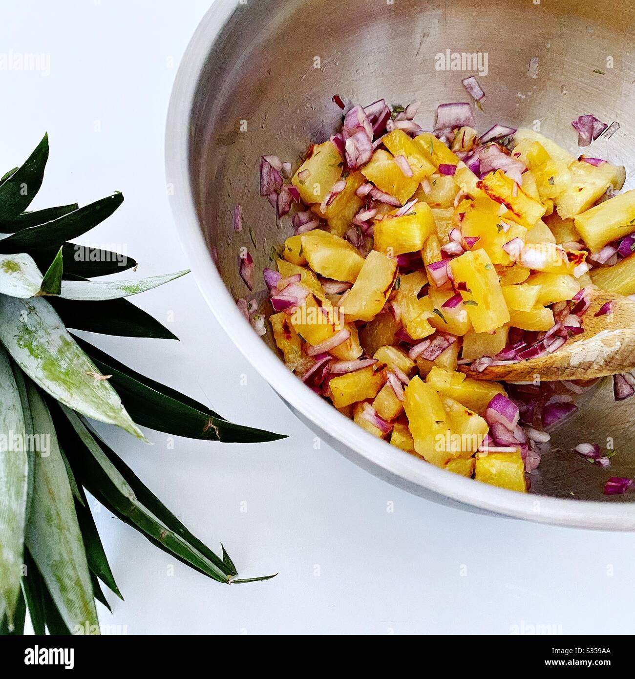 Preparing pineapple dish in the kitchen. Fresh and ripe fruit preparation. Ingredients for homemade pineapple salsa. Chargrilled chunks with red onion, lime juice and coriander in a steel mixing bowl. - Smartphone Captured Stock Image