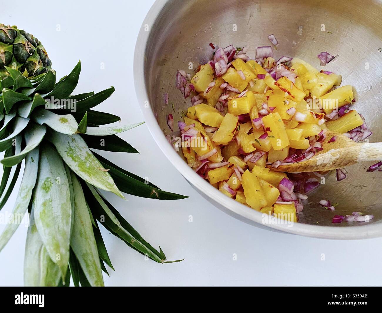 Preparing pineapple dish in the kitchen. Fresh and ripe fruit preparation. Ingredients for homemade pineapple salsa. Chargrilled chunks with red onion, lime juice and coriander in a steel mixing bowl. - Smartphone Captured Stock Image