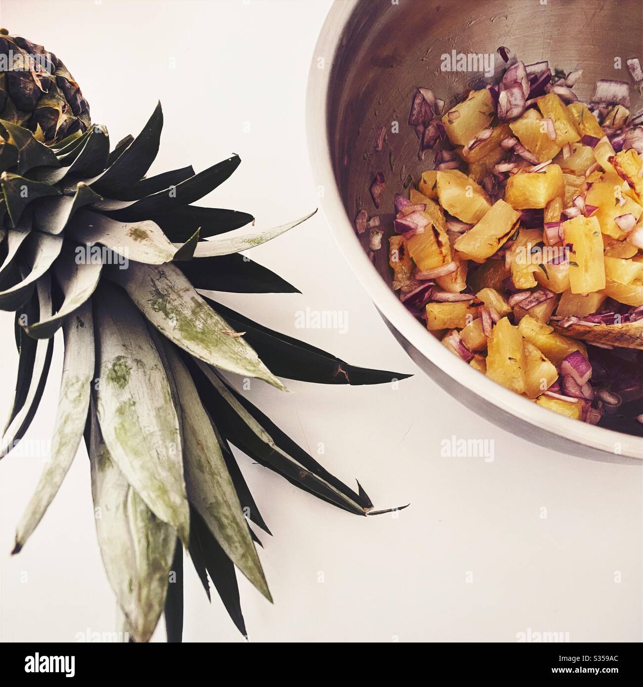 Preparing pineapple dish in the kitchen. Fresh and ripe fruit preparation. Ingredients for homemade pineapple salsa. Chargrilled chunks with red onion, lime juice and coriander in a steel mixing bowl. Stock Photo