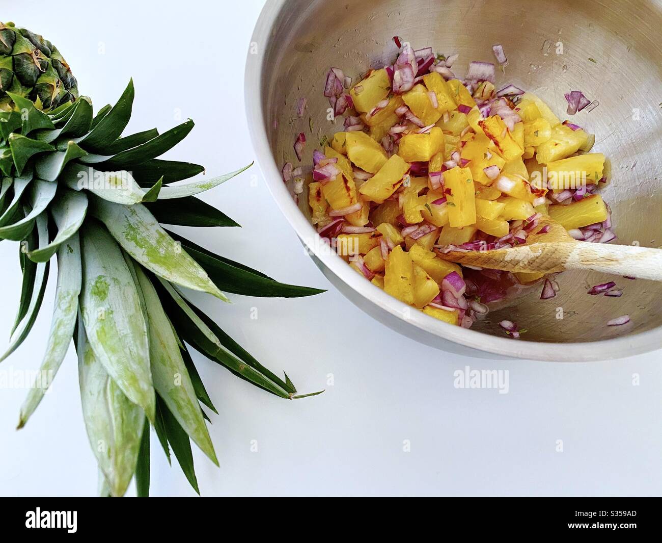 Preparing pineapple dish in the kitchen. Fresh and ripe fruit preparation. Ingredients for homemade pineapple salsa. Chargrilled chunks with red onion, lime juice and coriander in a steel mixing bowl. - Smartphone Captured Stock Image