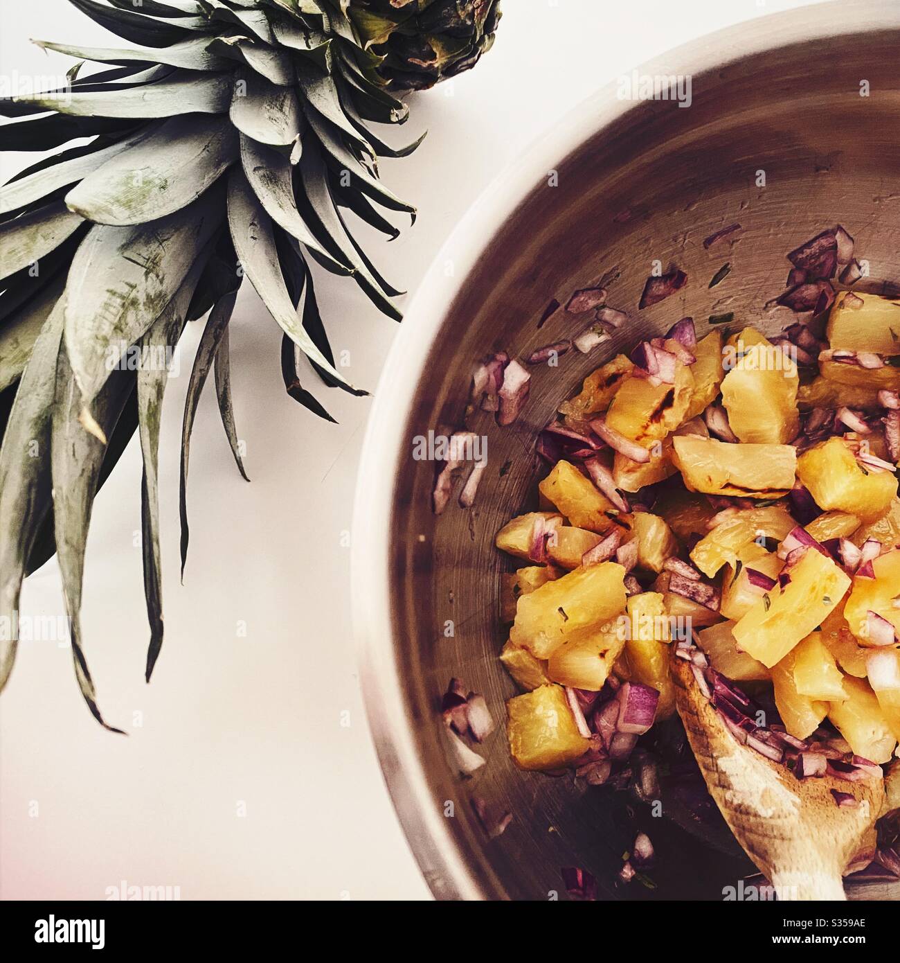 Preparing pineapple dish in the kitchen. Fresh and ripe fruit preparation. Ingredients for homemade pineapple salsa. Chargrilled chunks with red onion, lime juice and coriander in a steel mixing bowl. - Smartphone Captured Stock Image