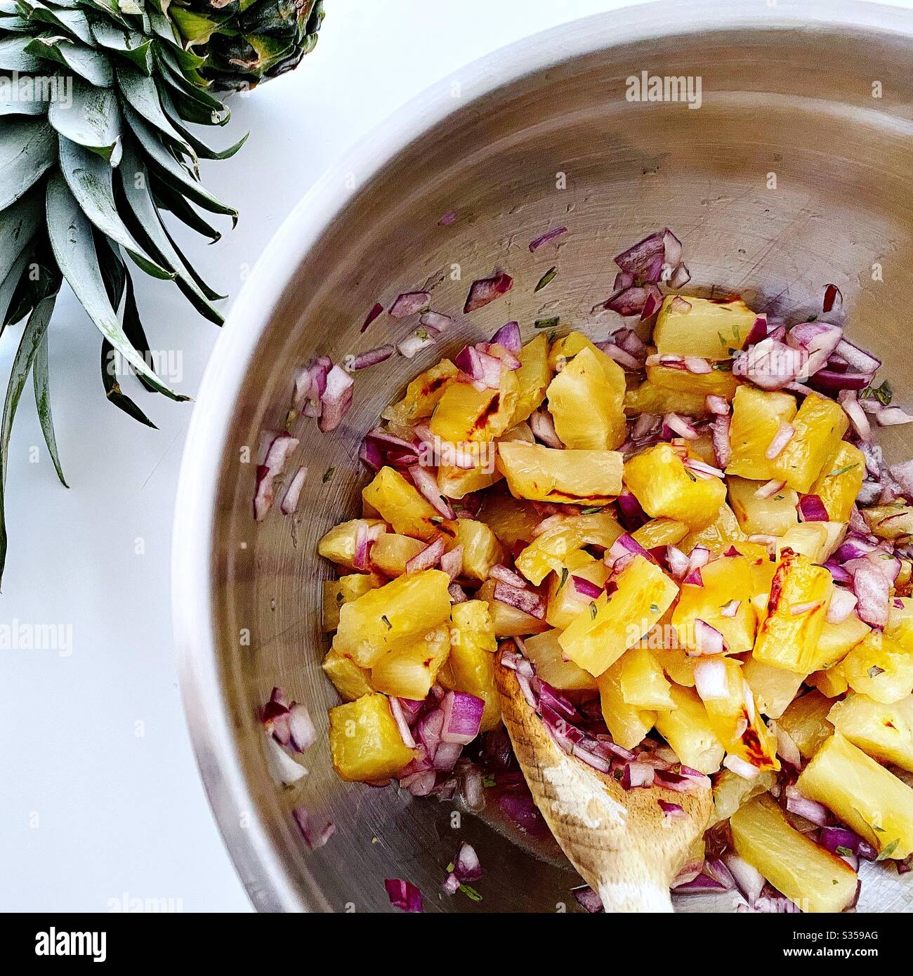 Preparing pineapple dish in the kitchen. Fresh and ripe fruit preparation. Ingredients for homemade pineapple salsa. Chargrilled chunks with red onion, lime juice and coriander in a steel mixing bowl. - Smartphone Captured Stock Image