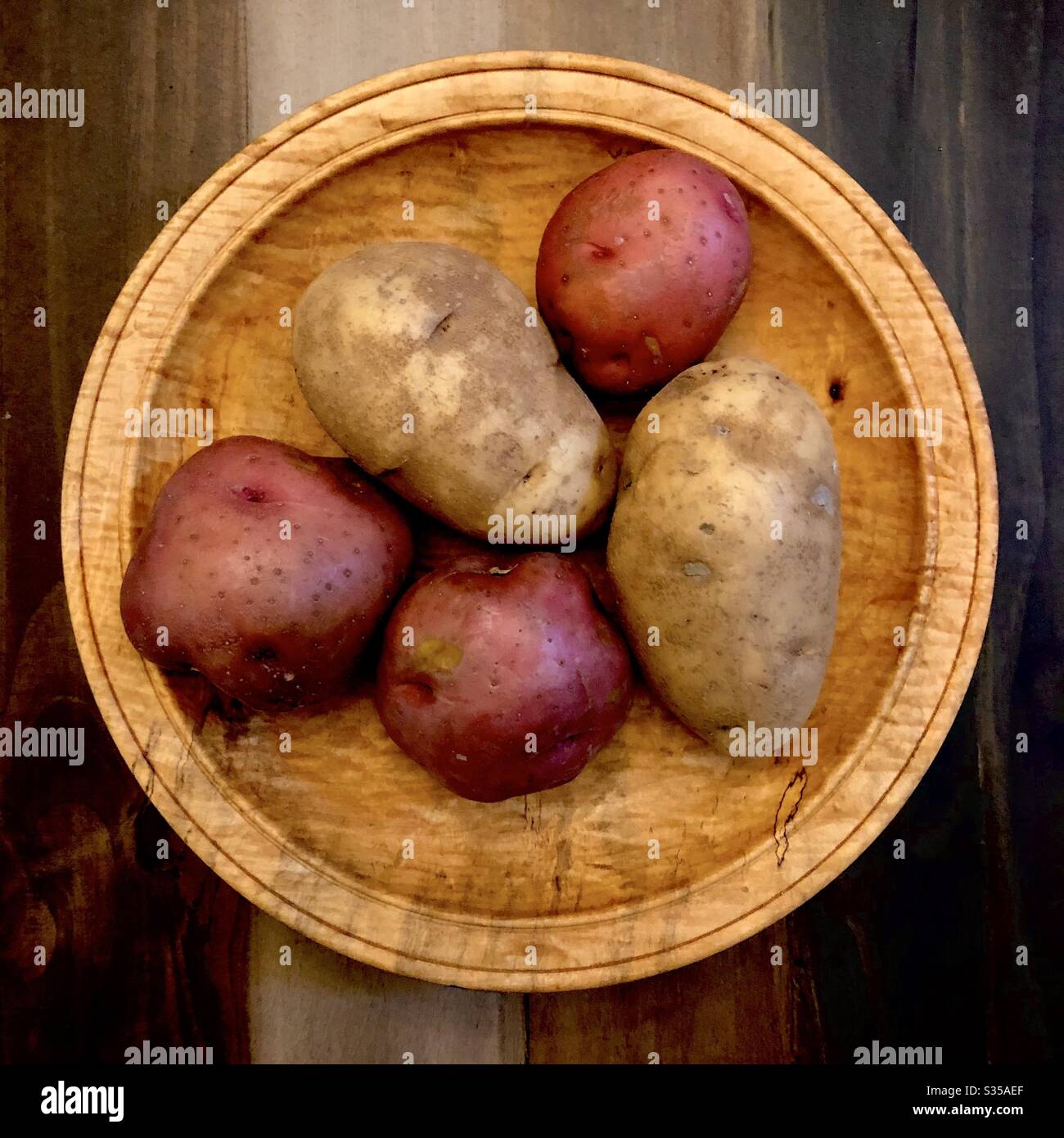 Still life of 3 red potatoes and 2 white potatoes in a wooden bowl. - Smartphone Captured Stock Image