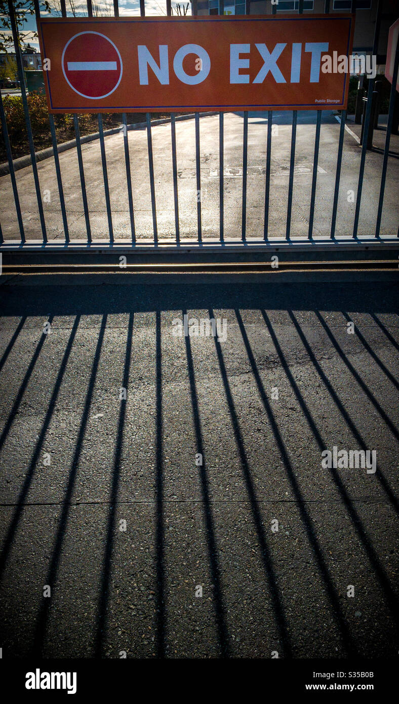 No Exit sign hung on bars of metal gate with dark shadows in foreground, late afternoon - Smartphone Captured Stock Image
