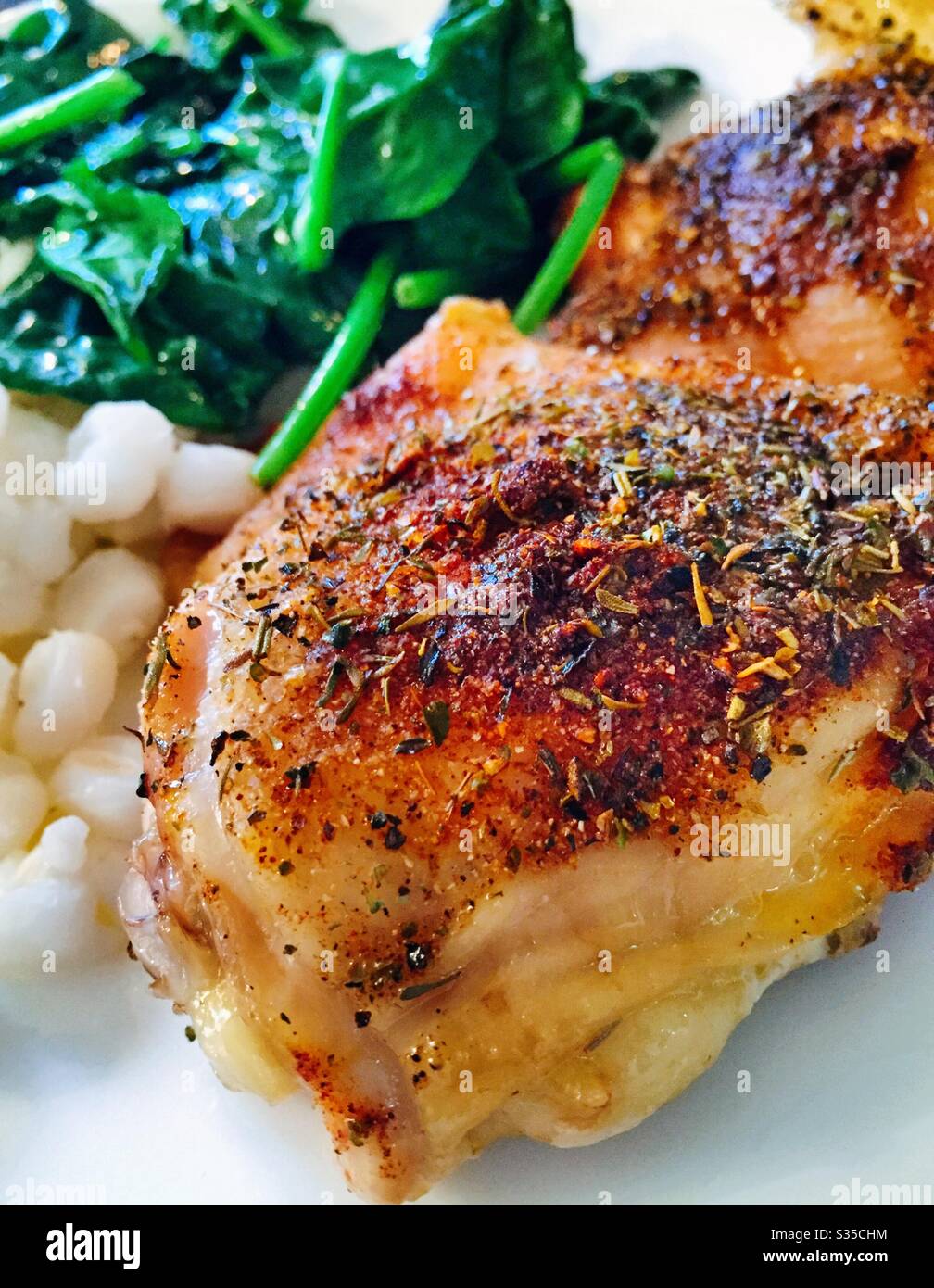 Close up of a balanced meal of baked chicken thighs sautéed spinach and hominy grits Stock Photo