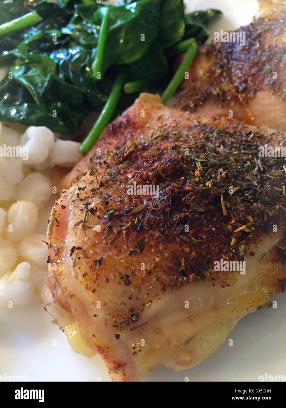 Close up of a balanced meal of chicken thighs sautéed spinach and hominy grits Stock Photo