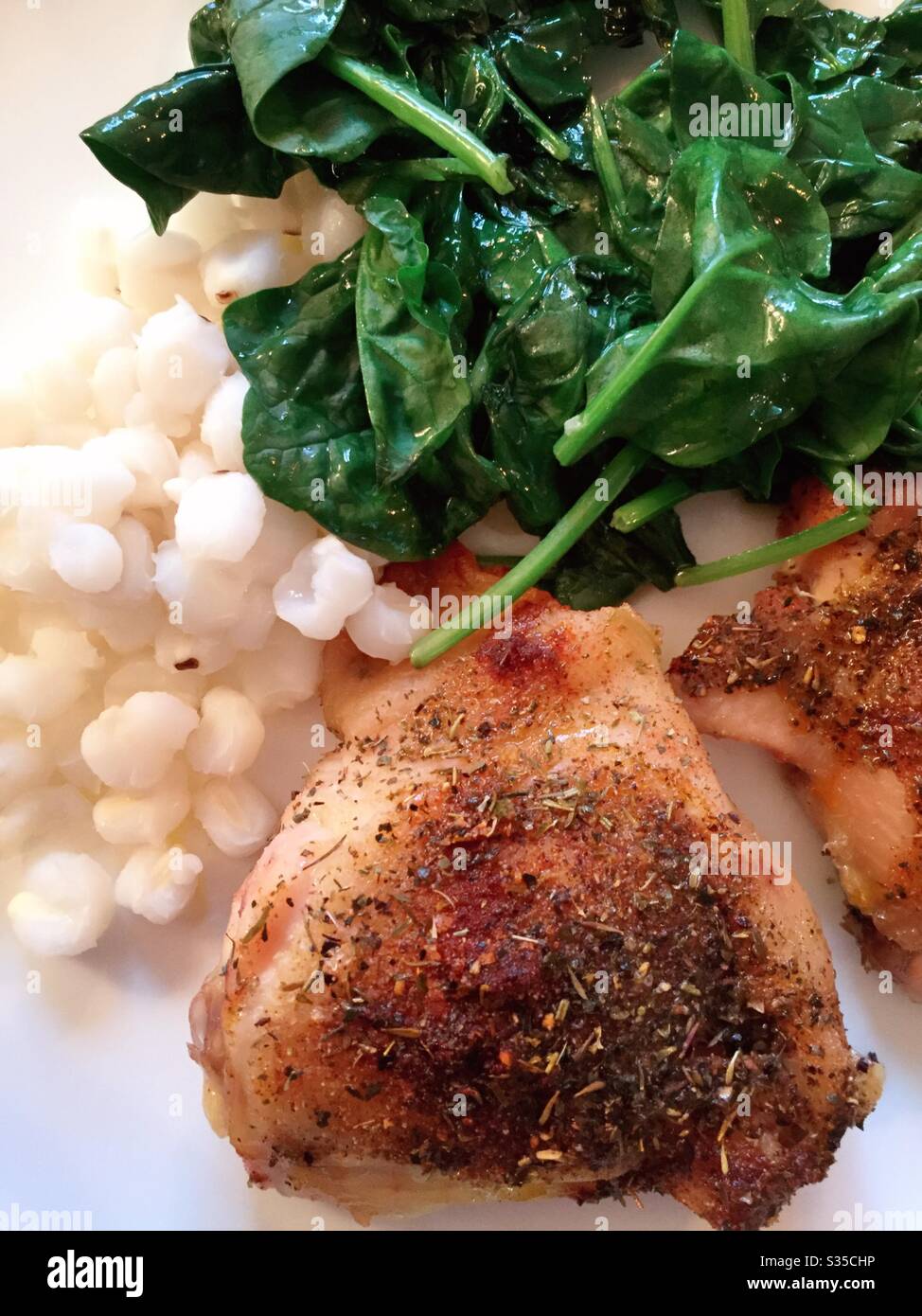 Close up of a balanced meal of the baked chicken thigh, Hominy grits and sautéed spinach Stock Photo