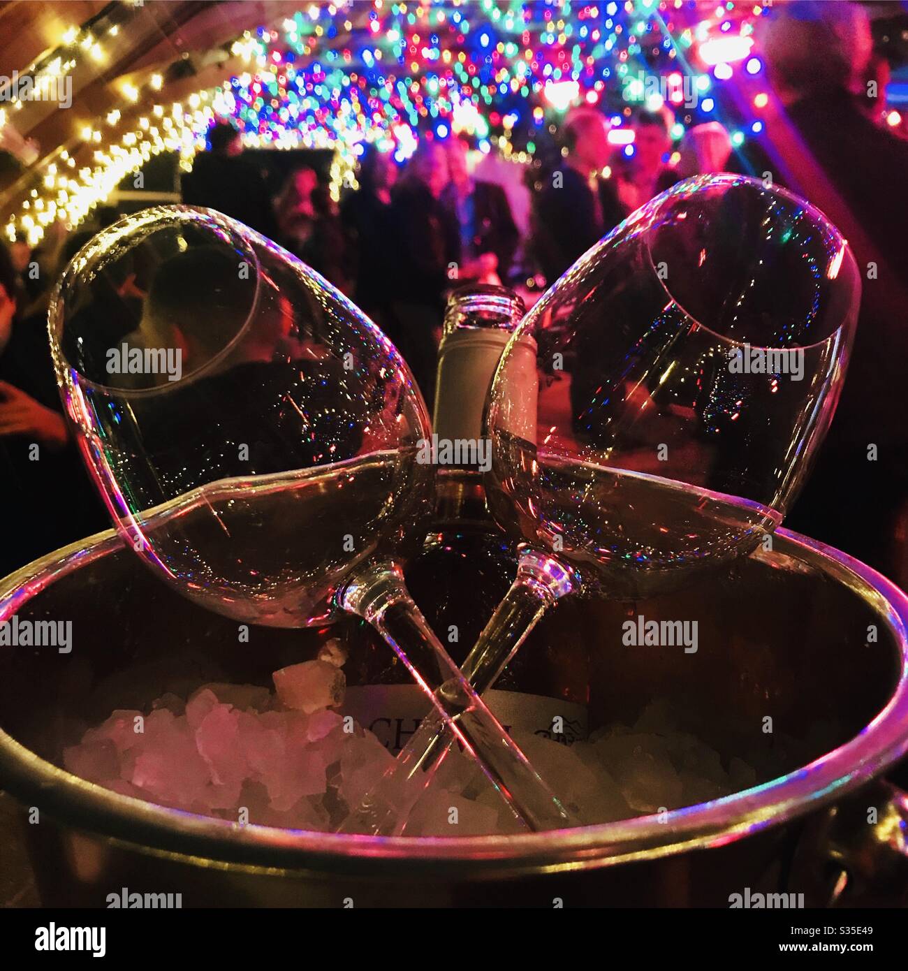 Wine and glasses in an ice bucket, under party lights Stock Photo
