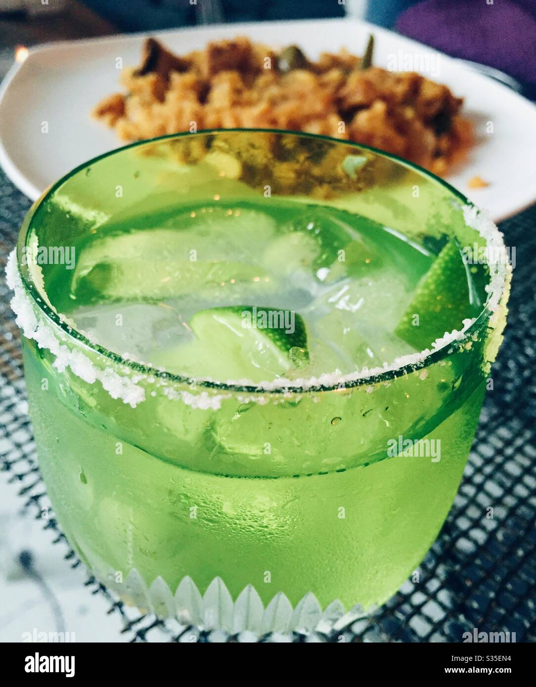 A margarita cocktail with a salted rim in front of a main course of Spanish paella Stock Photo