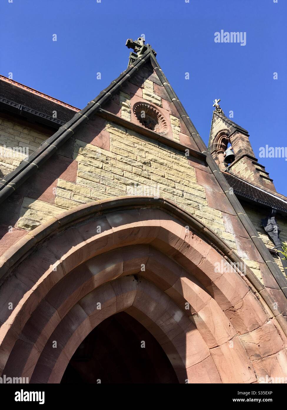 A sandstone church porch and arch,  and clock tower, under a bright blue sky Stock Photo