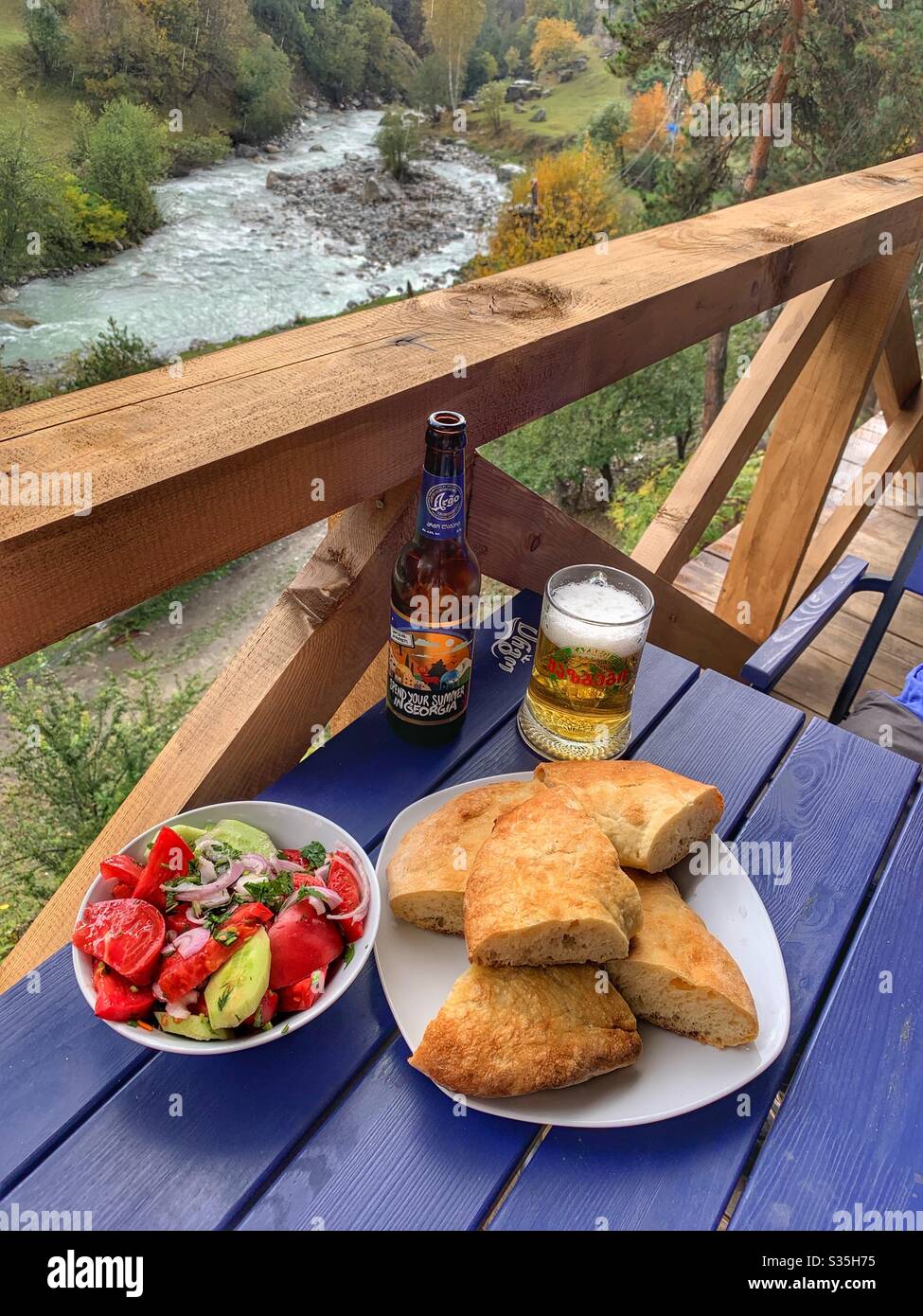 A typical Georgian meal of Bread, Salad and Beer, over looking a river. Mestia, Georgia. - Smartphone Captured Stock Image