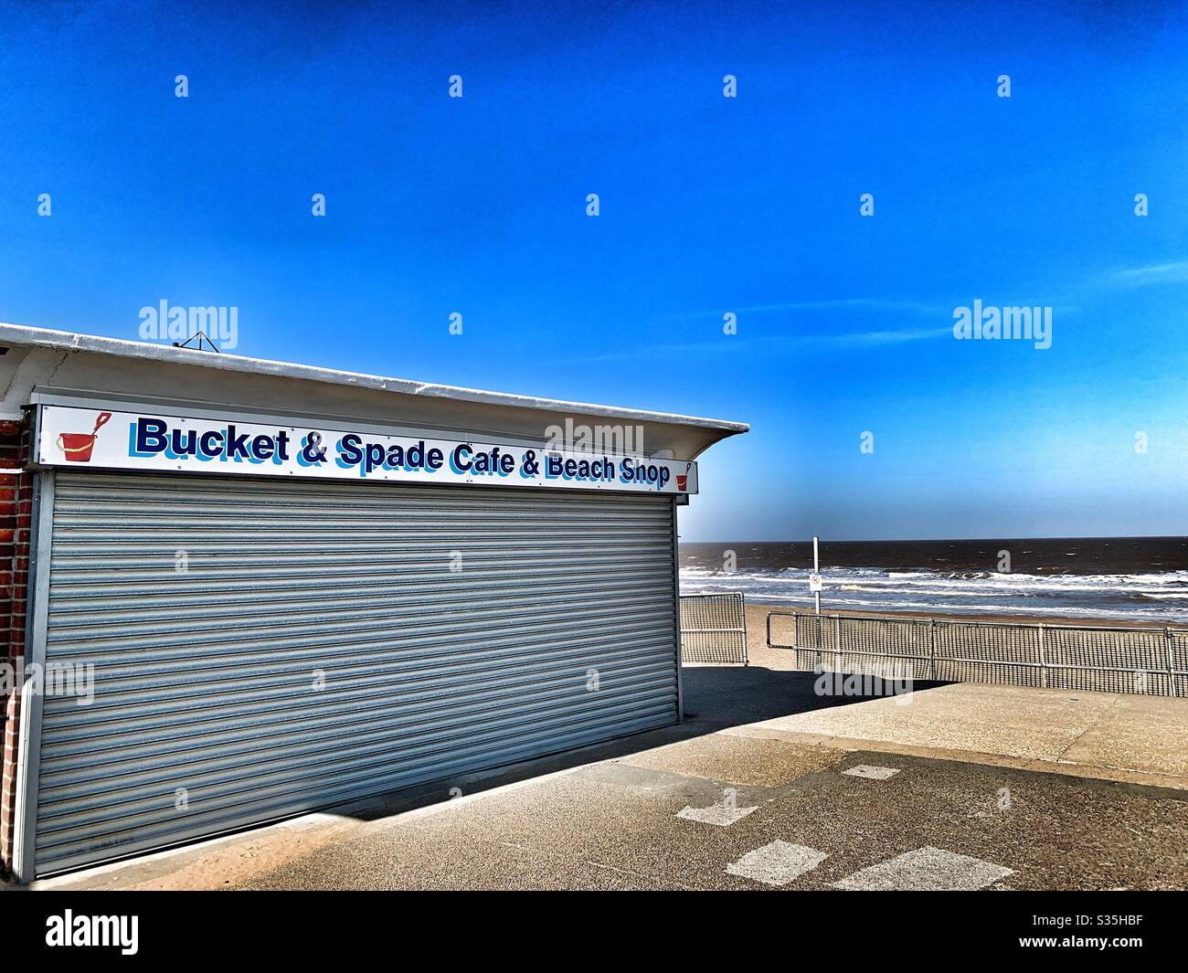 A beach shop with its shutters down beside a deserted beach in Mablethorpe, Lincolnshire due to the Coronavirus restrictions and lockdown Stock Photo