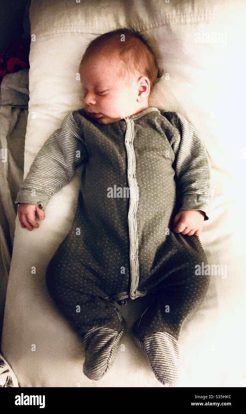 Newborn baby sleeping wearing a gray onesie suit. Stock Photo