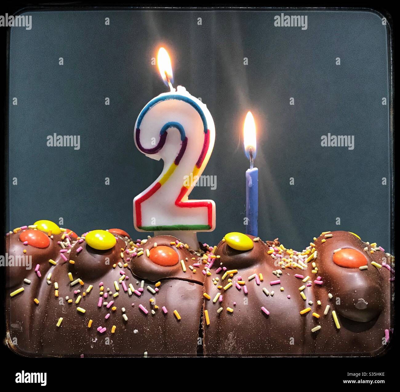 21st Birthday chocolate caterpillar cake with sprinkles and chocolate beans and 2 and 1 lit candles burning Stock Photo