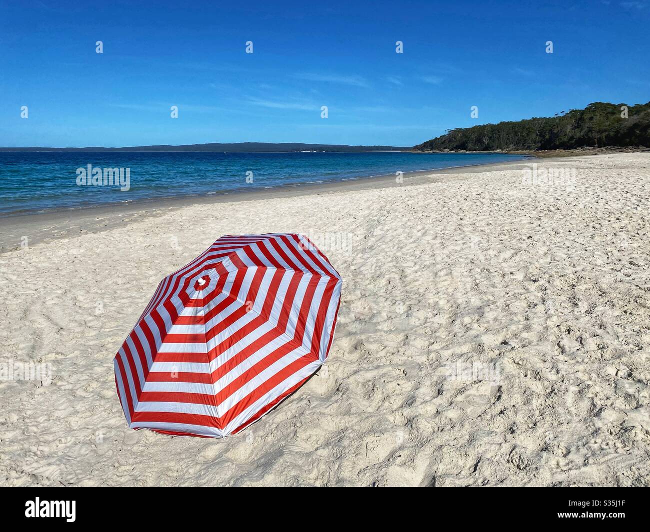 Beach umbrella on deserted white sandy beach. Concept - umbrella on empty beach awaits return of people after end of social distancing and self isolation caused by Coronavirus (return to normal life) Stock Photo