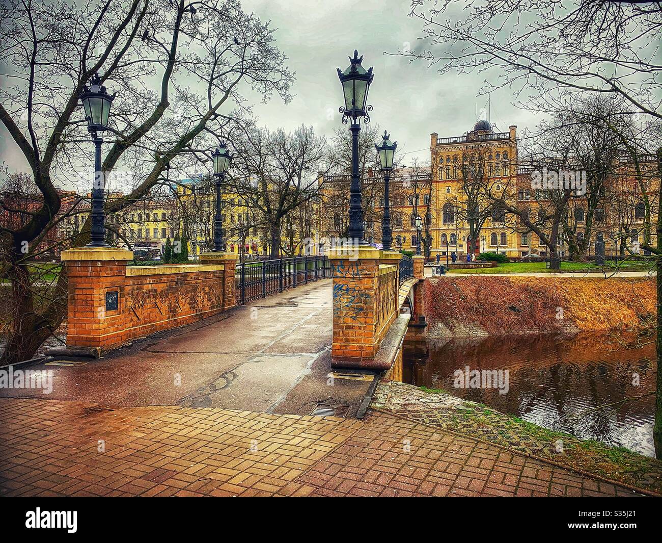 Bridge across the river, flanked by old fashioned ornate black lampposts. In the background as beautiful golden coloured historic buildings, which compliment the fridge. Trees.’ - Smartphone Captured Stock Image
