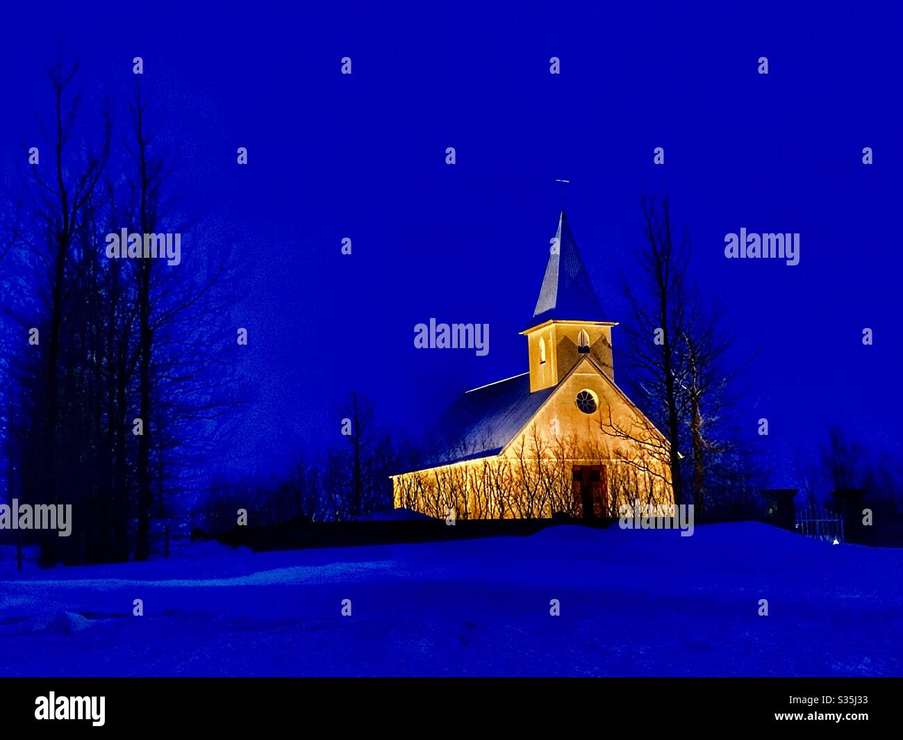 A simple Icelandic church in the middle of the snowy countryside, glowing in blue hour. - Smartphone Captured Stock Image