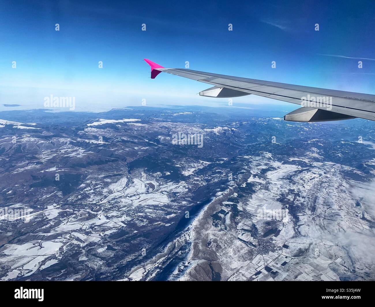 Wingtip photo. Wizz Air airplane flying over a vast snowy landscape in Europe. - Smartphone Captured Stock Image