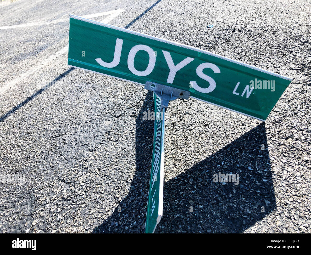 Street sign with road name for Joys Lane, knocked to the pavement with off-kilter and and angular shadows - Smartphone Captured Stock Image