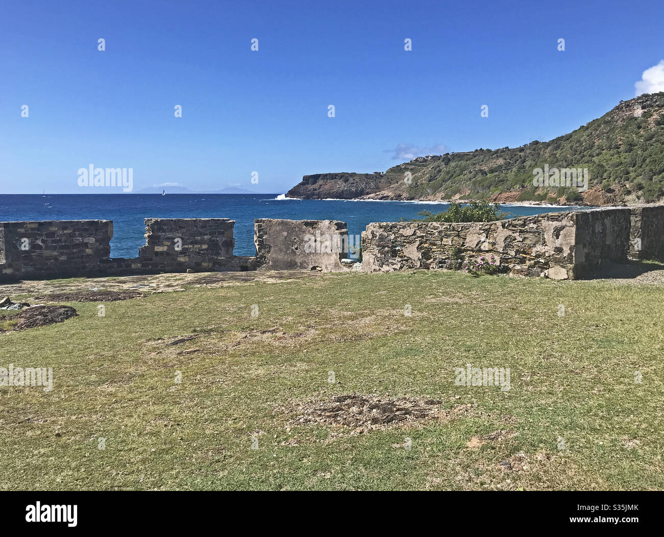 Antigua coastline and outer fort wall with cannon ports as seen from the Fort Berkeley Peninsula in Antigua and Barbuda, Caribbean, Lesser Antilles, West Indies with blue sky copy space. - Smartphone Captured Stock Image